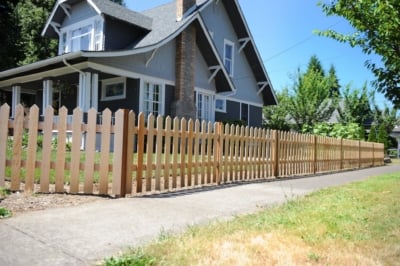 1002 Fencing Cedar Picket A cedar picket fence running along a sidewalk with a house in the background.
