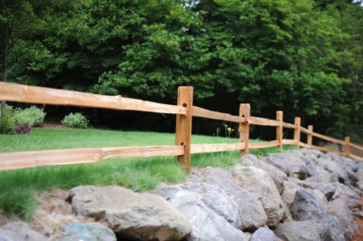 1012 Cedar Split Rail Fencing A cedar split rail fence over rocks with trees in the background.
